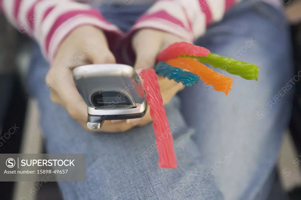 Hispanic teenaged girl holding cell phone and candy