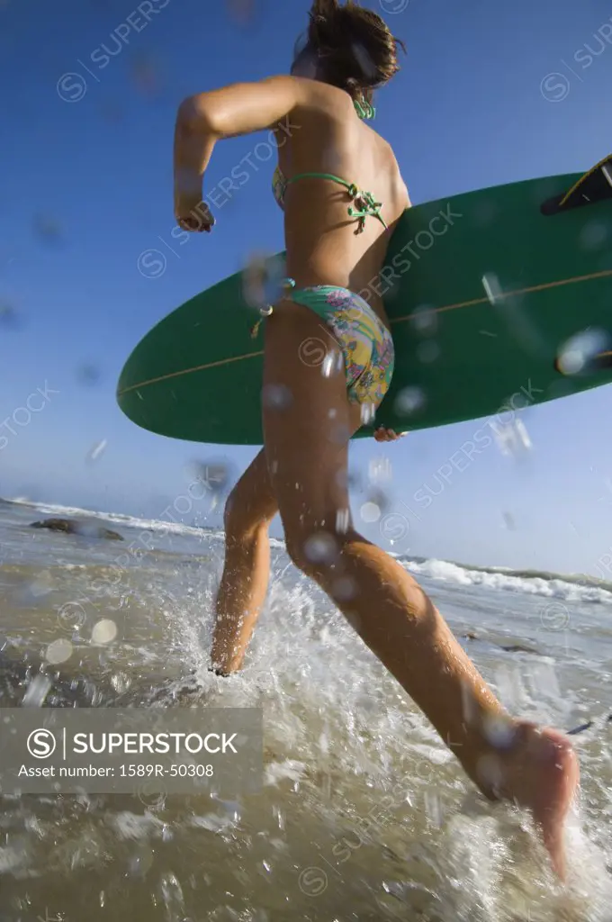Hispanic girl running with surfboard