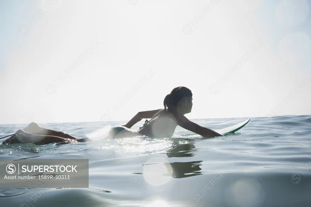 Hispanic girl paddling on surfboard