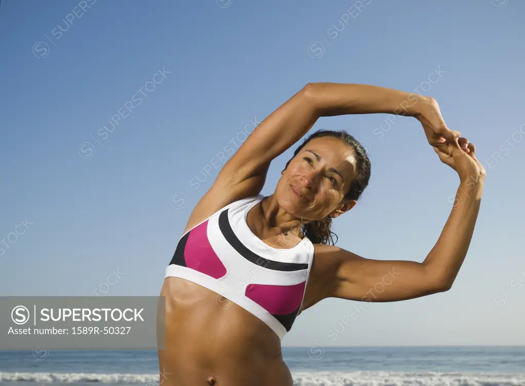 Hispanic woman stretching at beach