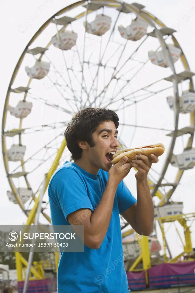 Mixed Race teenaged boy eating hot dog at carnival