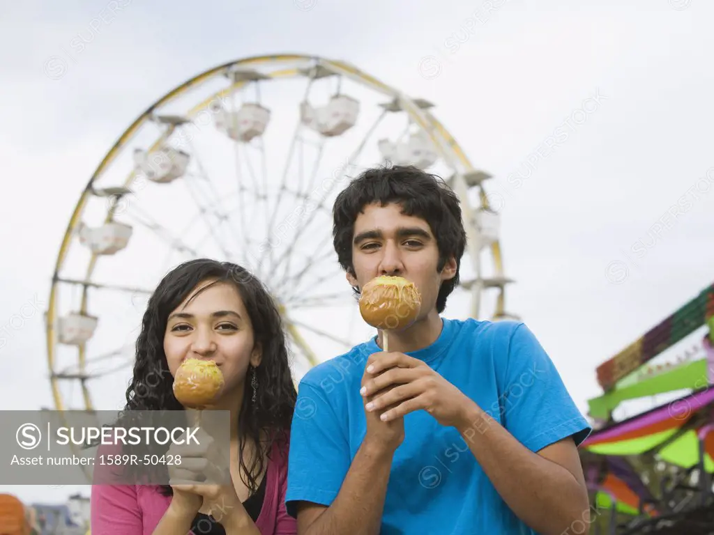 Multi-ethnic teenaged couple eating candied apples