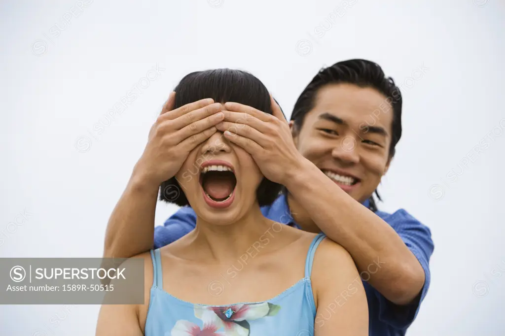 Asian man covering girlfriends eyes