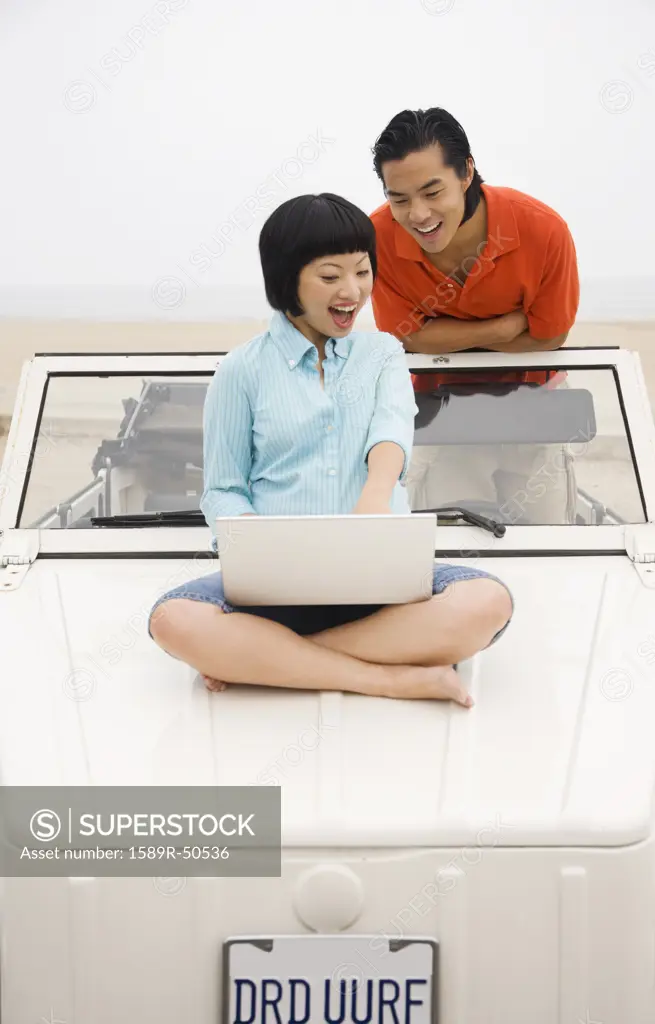 Asian couple looking at laptop on car