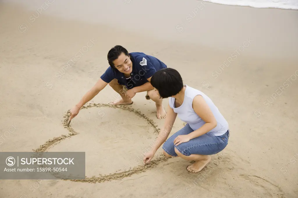 Asian couple drawing heart in sand