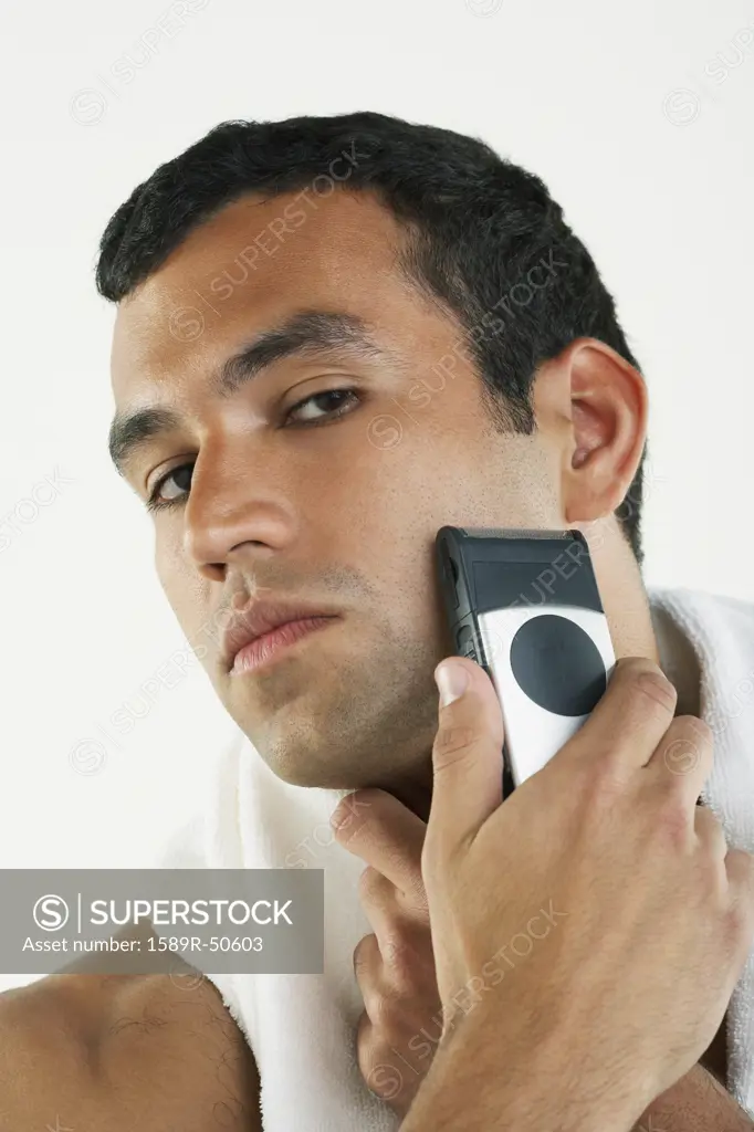 Hispanic man shaving face with electric razor