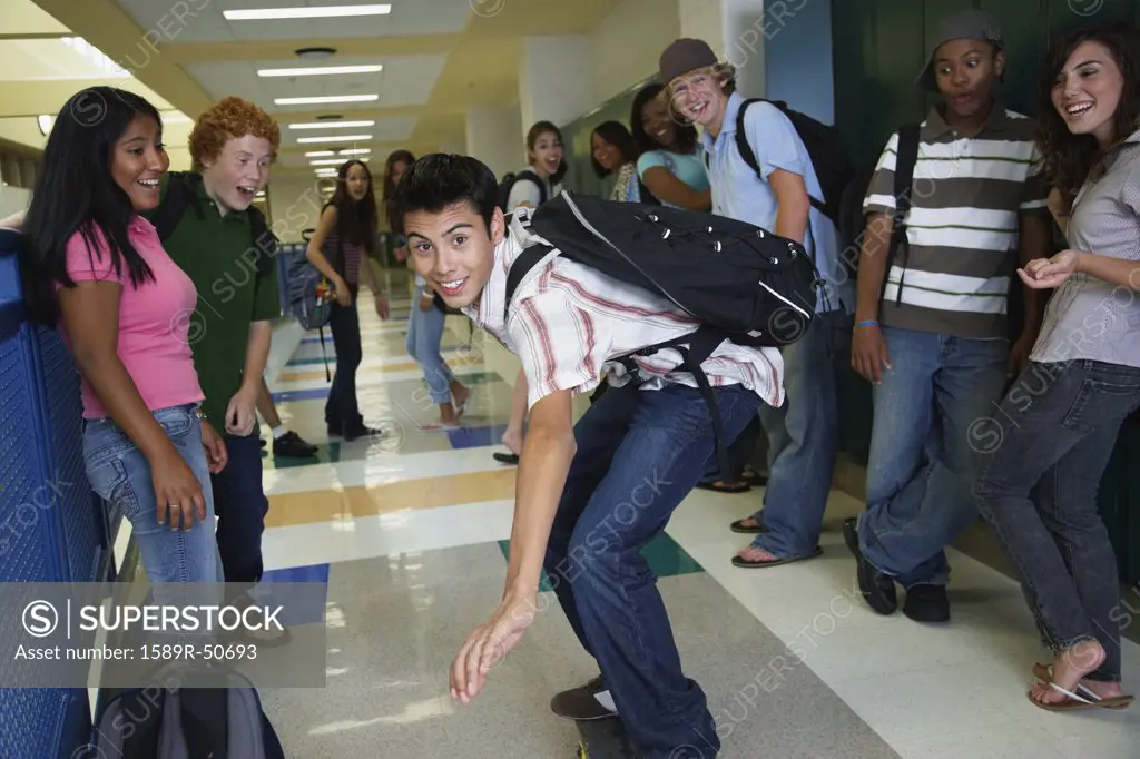 Hispanic teenaged boy riding skateboard in school hallway