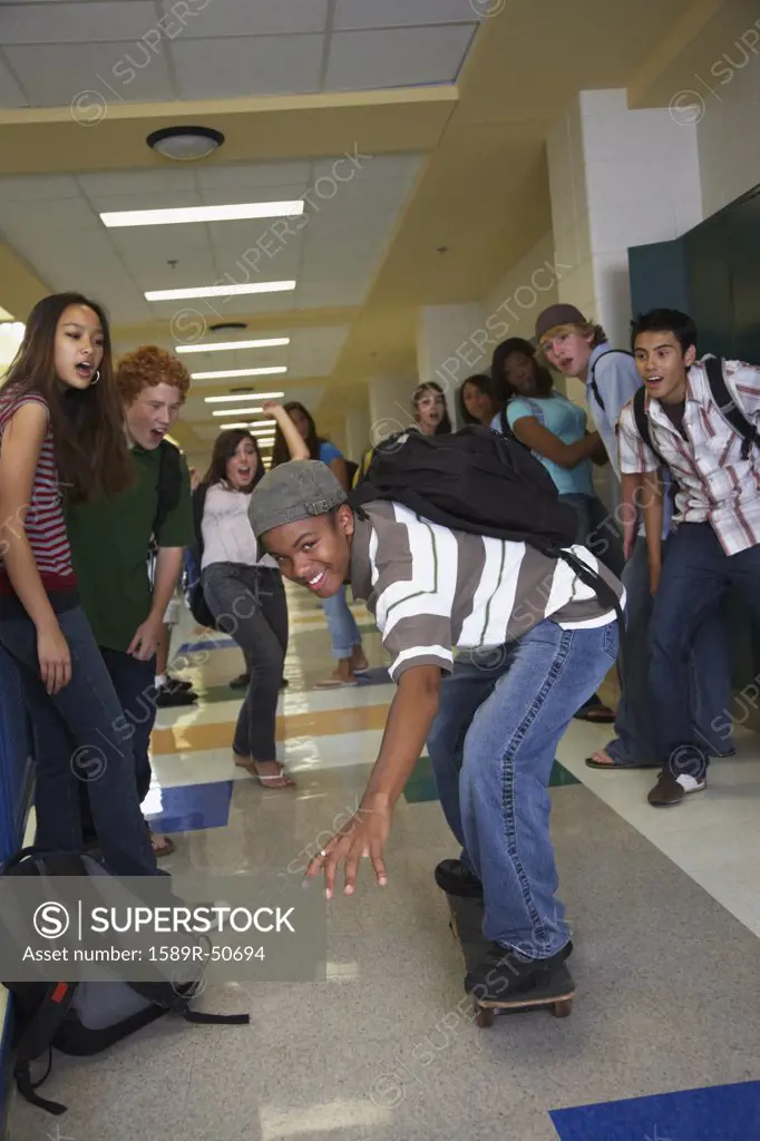 African American teenaged boy riding skateboard in school hallway