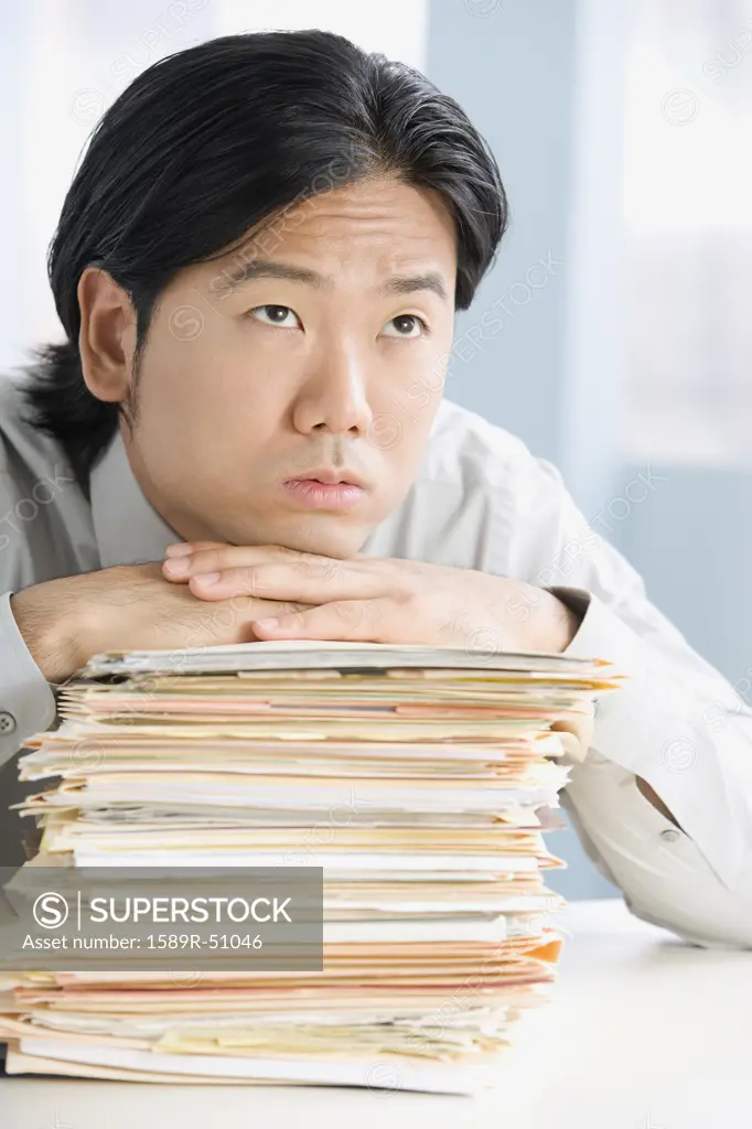 Asian businessman leaning on stack of paperwork