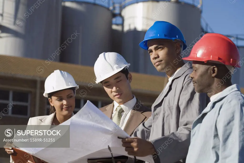 Multi-ethnic businesspeople and construction workers looking at blueprints