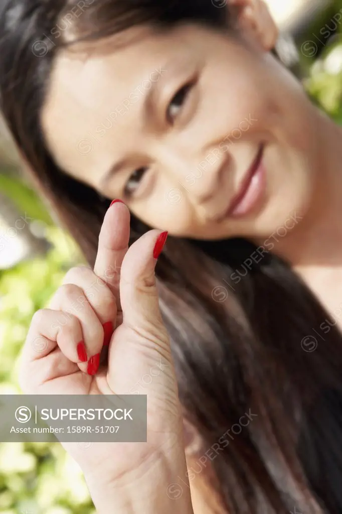 Asian woman holding out thumb and index finger