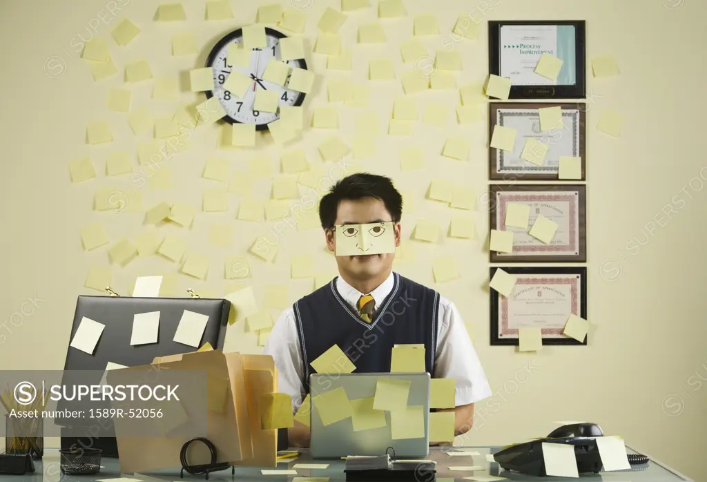 Asian businessman with sticky notes all over wall and face