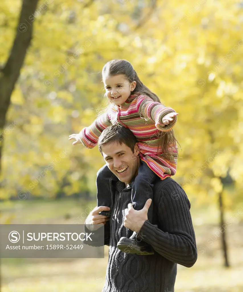 Hispanic father holding daughter on shoulders