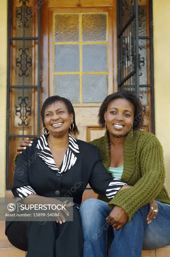African mother and adult daughter sitting on porch steps