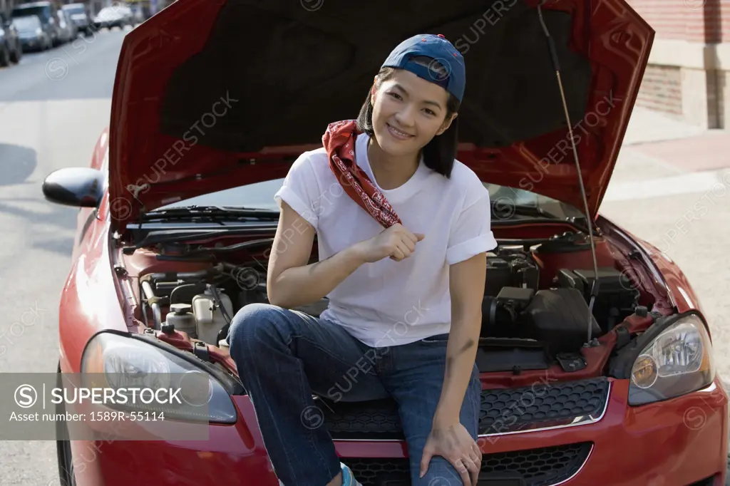 Asian woman sitting next to open car hood
