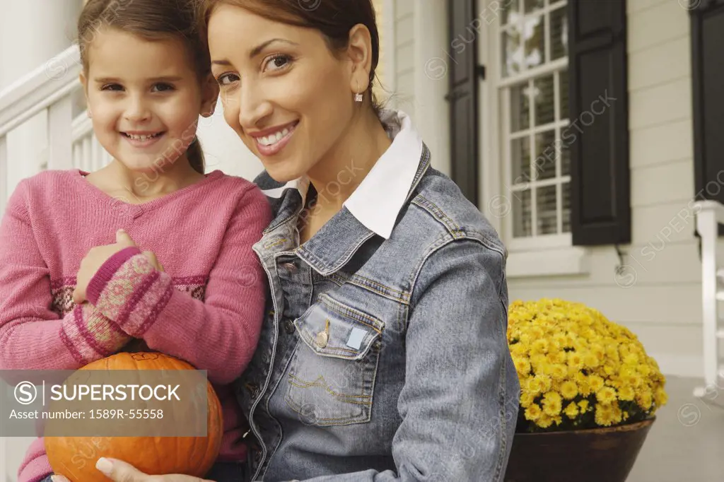 Hispanic mother and daughter holding pumpkin