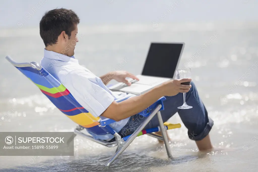 Hispanic man in beach chair with laptop 