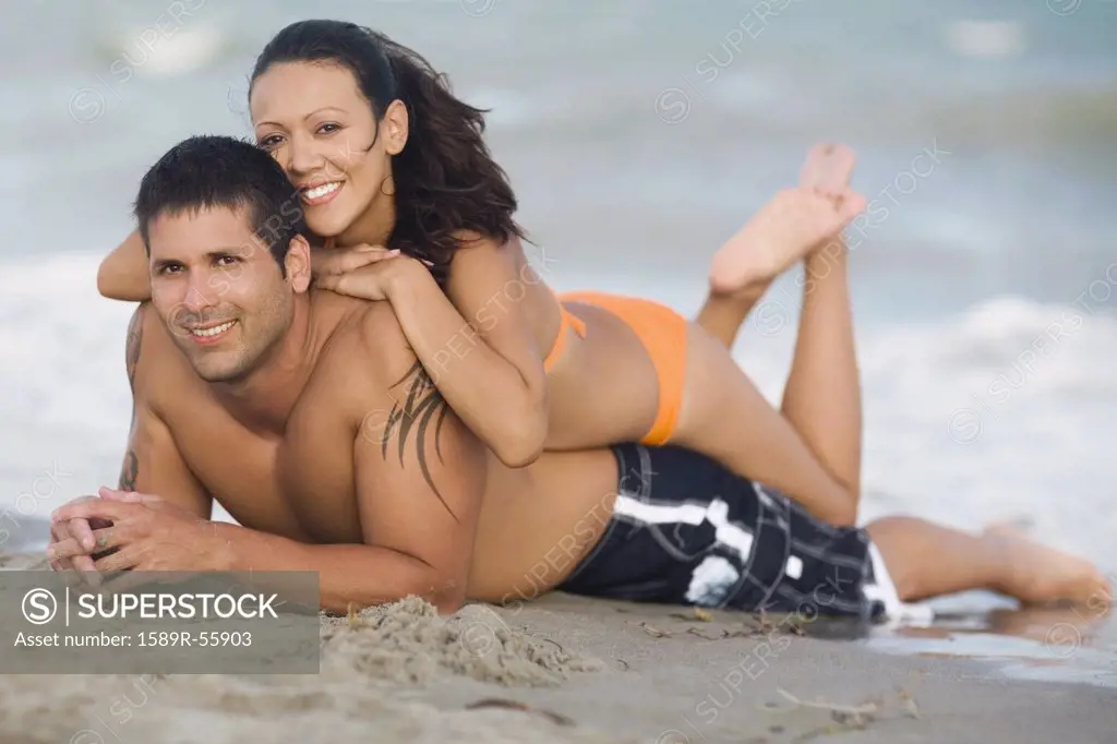 Hispanic couple laying on beach