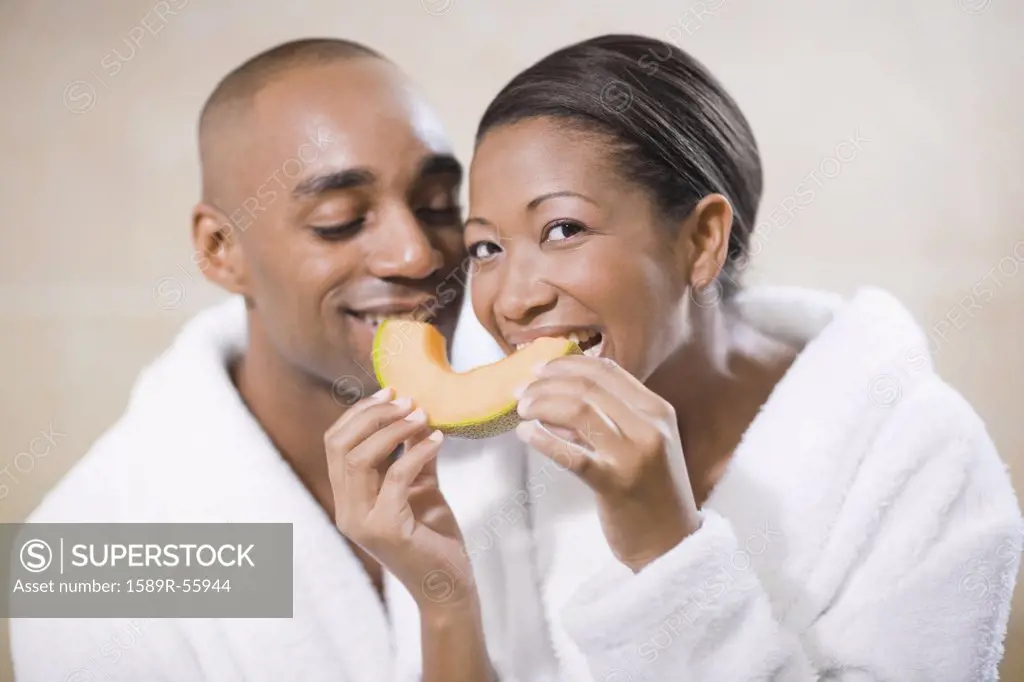 African couple in bathrobes eating melon