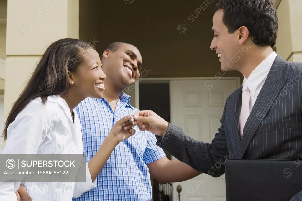 Hispanic real estate agent handing house key to African couple