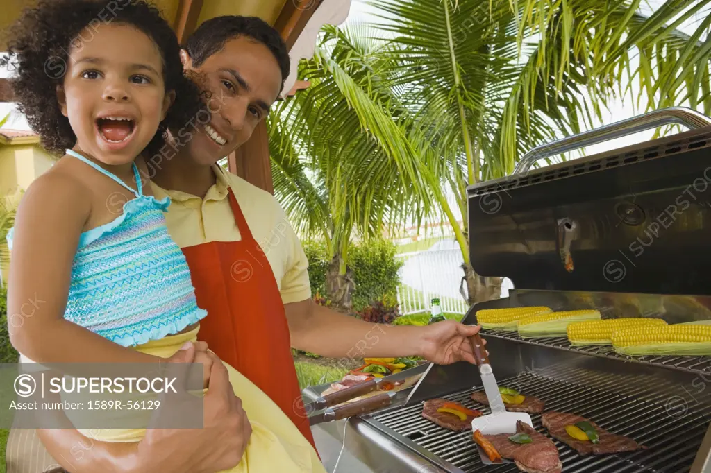 Hispanic father and daughter barbecuing
