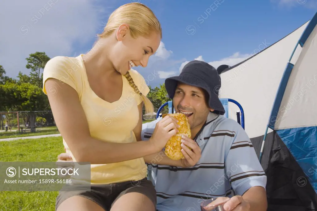 Hispanic woman feeding sandwich to boyfriend