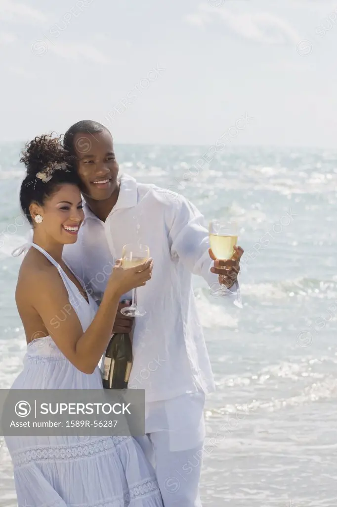 Multi-ethnic couple drinking wine at beach