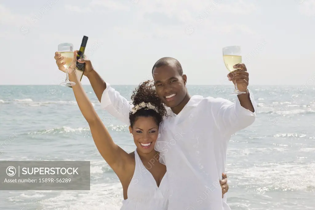 Multi-ethnic couple holding wine at beach