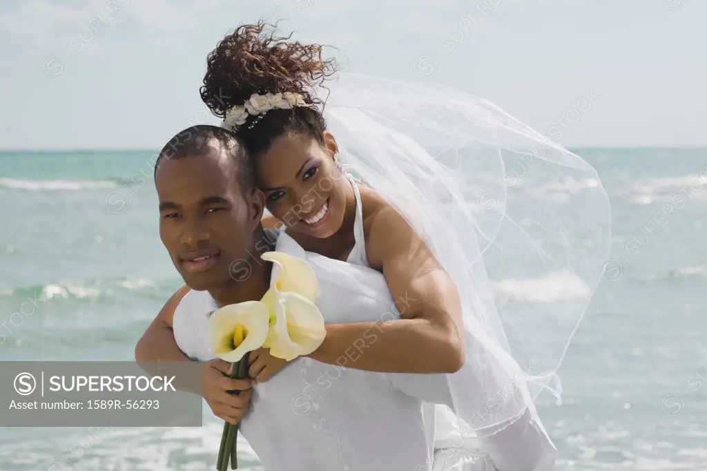 Multi-ethnic bride and groom hugging at beach