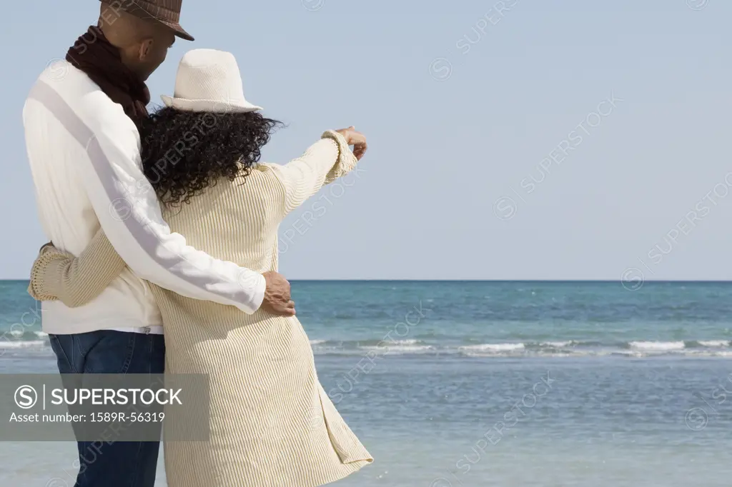 Multi-ethnic couple hugging and pointing at beach