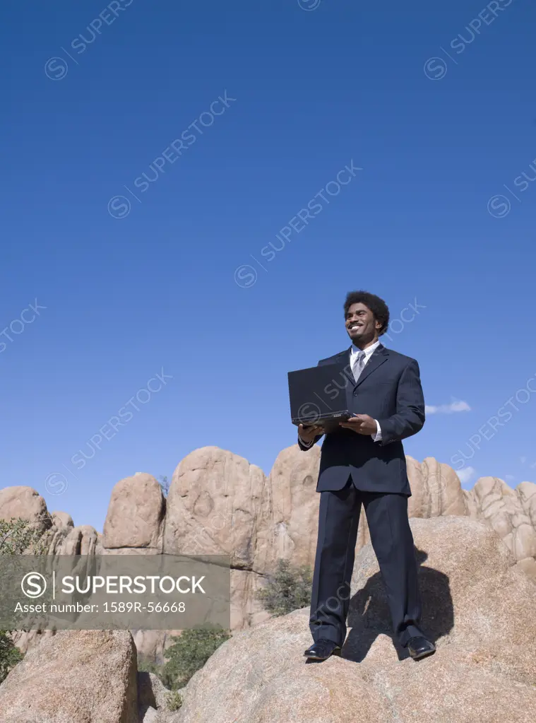 African businessman standing on rock holding laptop