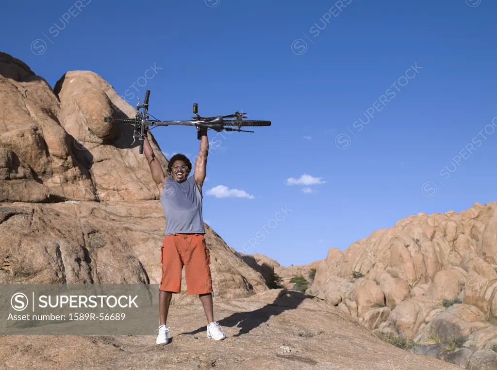 African man holding mountain bike over head