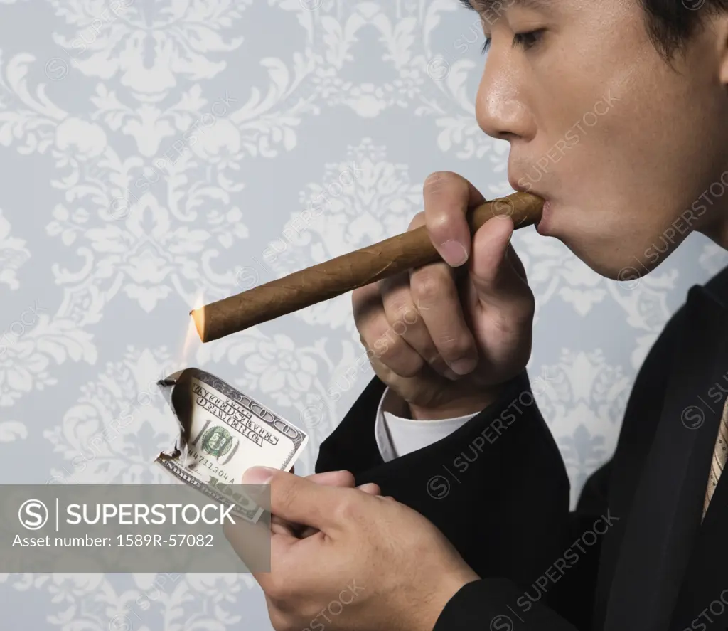 Asian man lighting cigar with money
