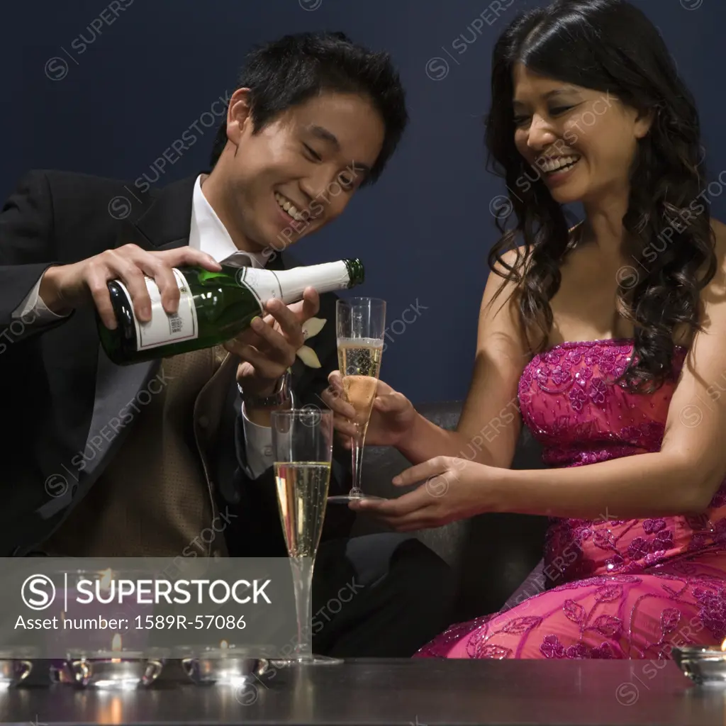 Asian man pouring champagne for girlfriend