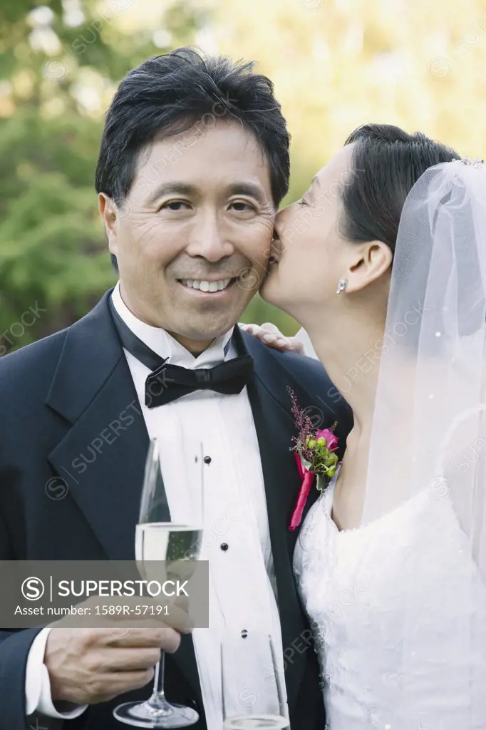 Asian bride kissing grooms cheek