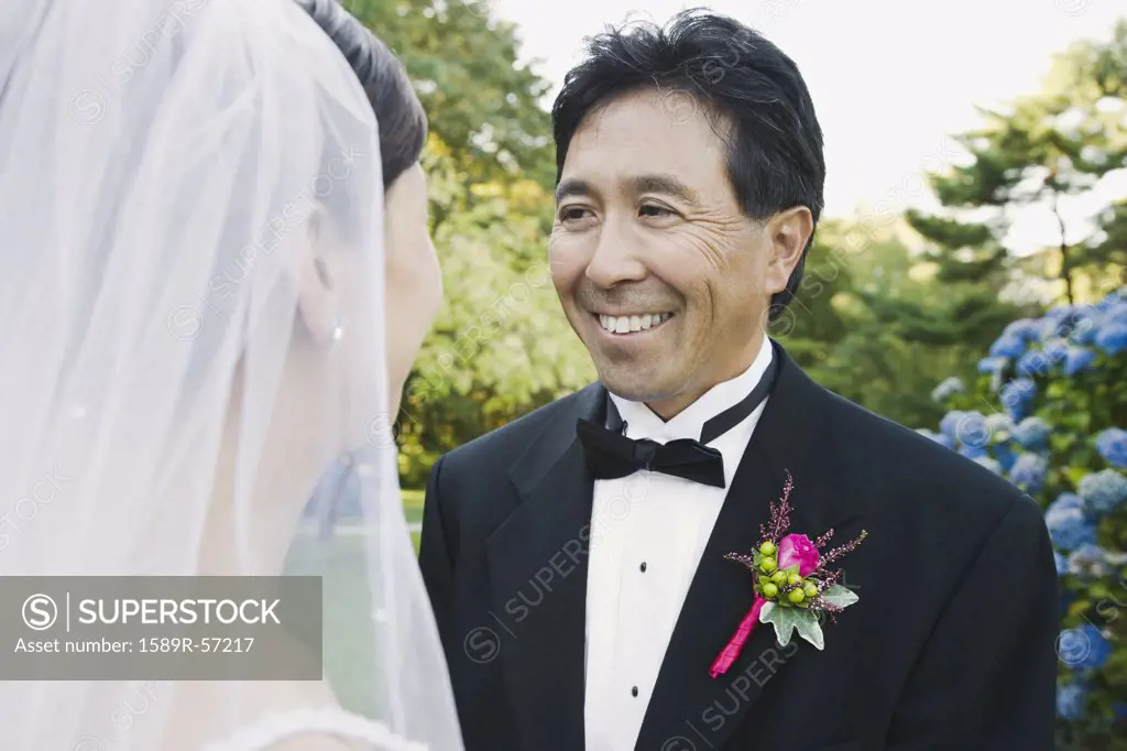 Asian groom smiling at bride