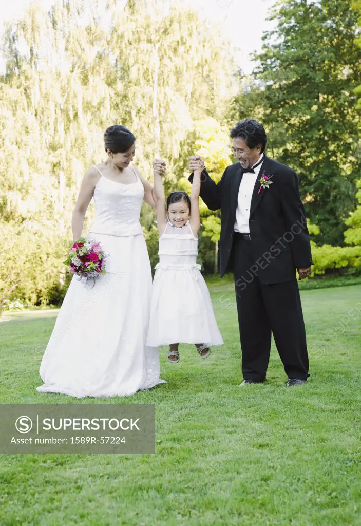 Asian newlyweds holding flower girls hands
