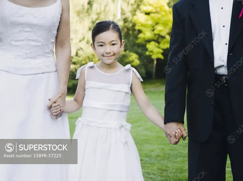 Asian newlyweds holding flower girls hands