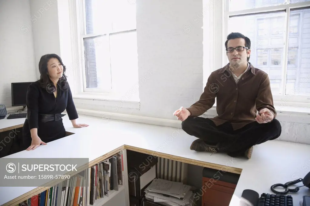 Hispanic businessman meditating next to coworker