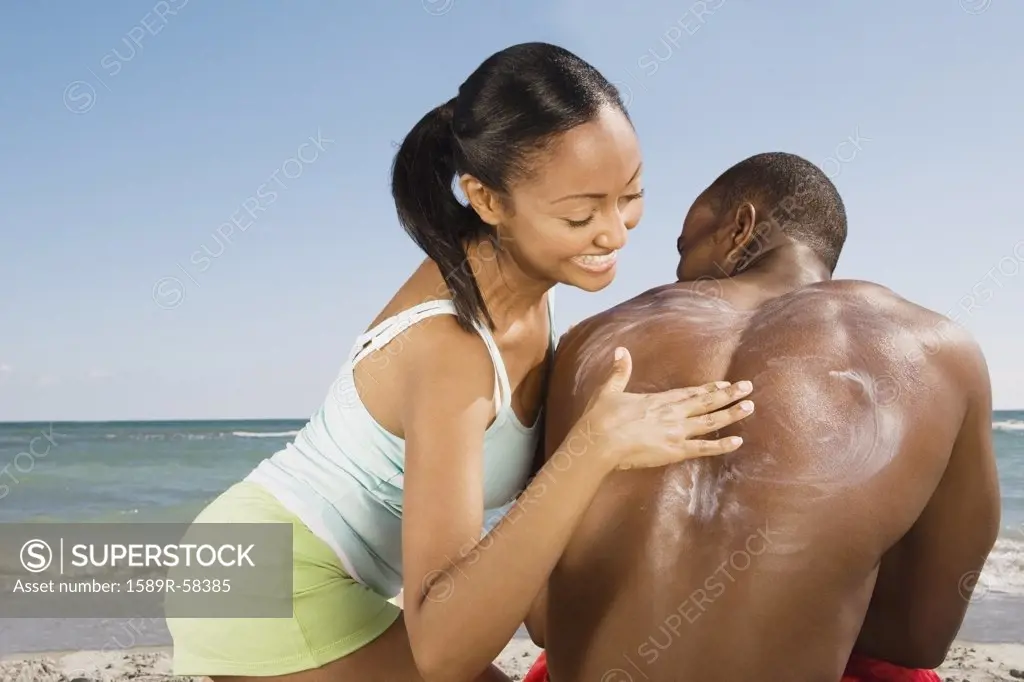 Hispanic woman rubbing sunscreen on boyfriends back
