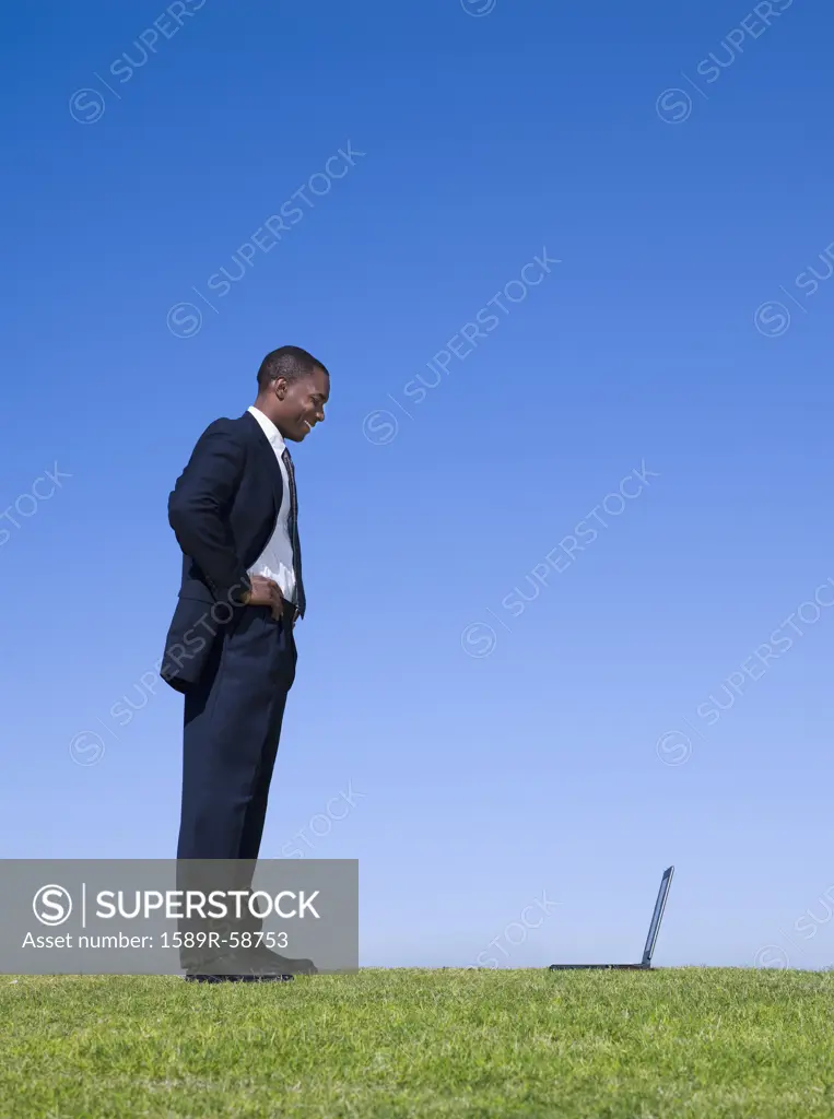 African businessman looking at laptop in grass