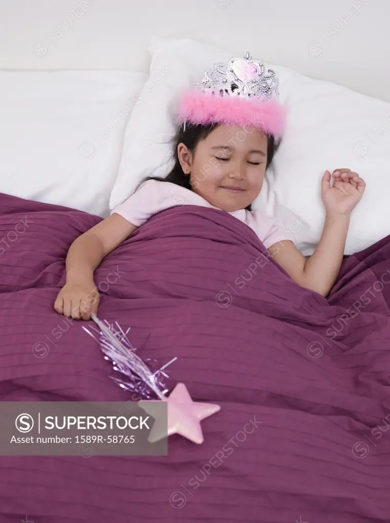 Eurasian girl wearing tiara in bed