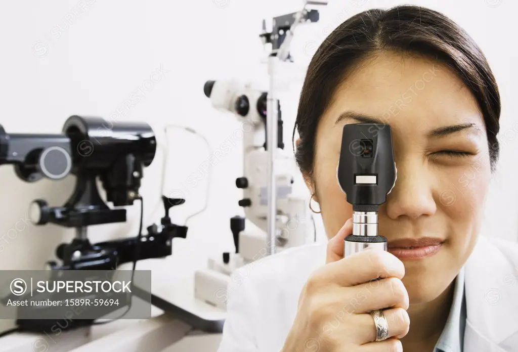 Asian female optometrist looking through equipment
