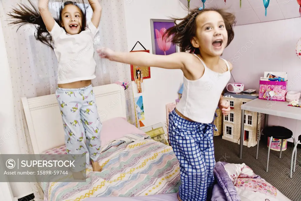 Asian sisters jumping on bed