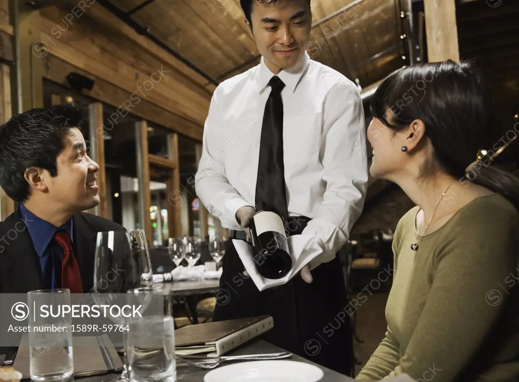 Asian waiter showing wine to couple