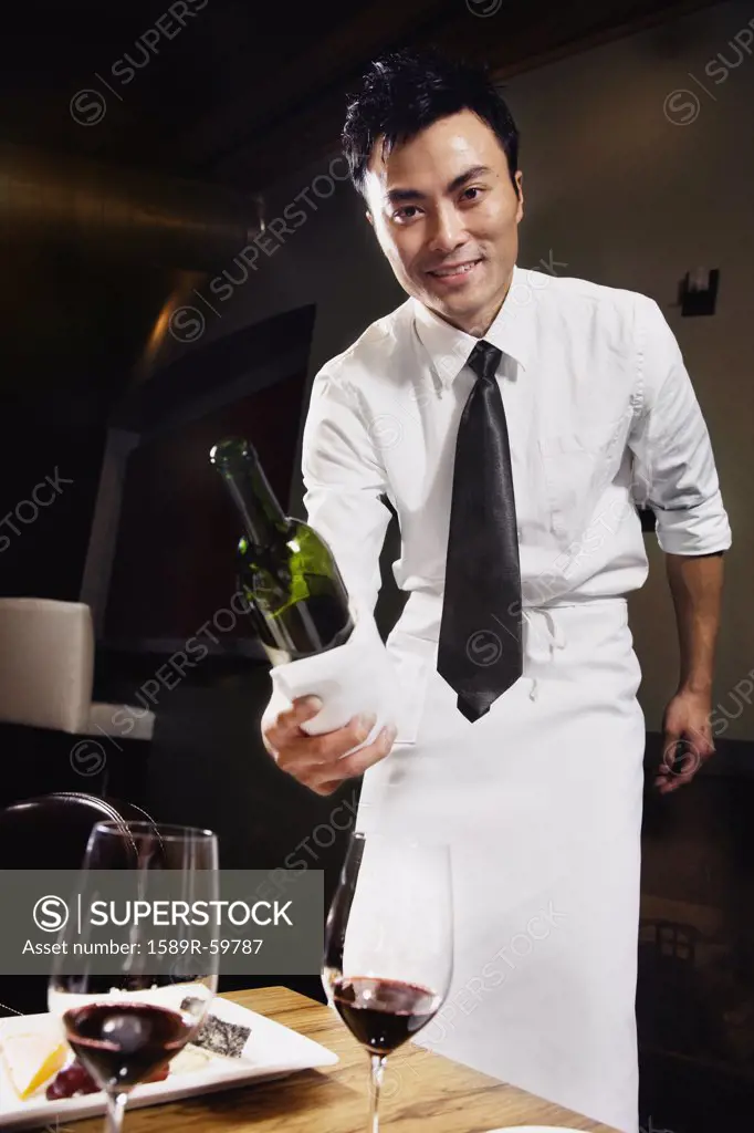 Asian waiter pouring wine