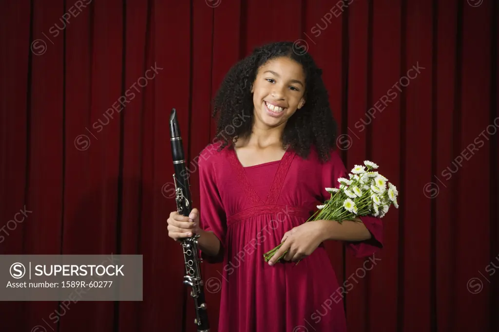 Mixed Race girl holding clarinet and flowers on stage