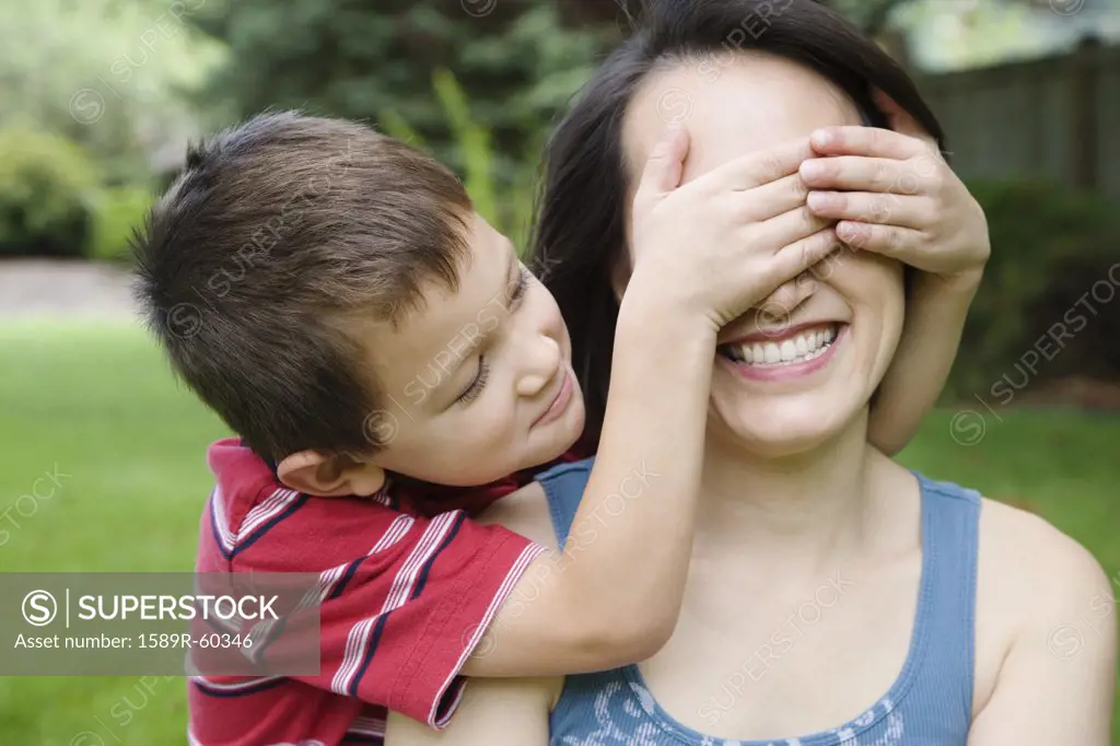Asian boy covering mothers eyes