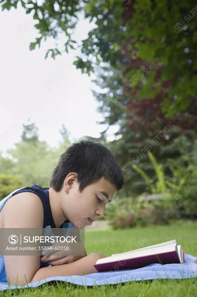 Asian boy reading in grass