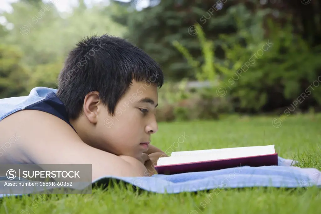 Asian boy reading in grass